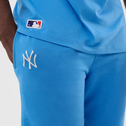 New Era New York Yankees MLB League Essential Pastel Blue Shorts, close-up side view showing the white embroidered NY logo on the left thigh, a small MLB logo on the matching shirt above the shorts, and the pastel blue fabric design.