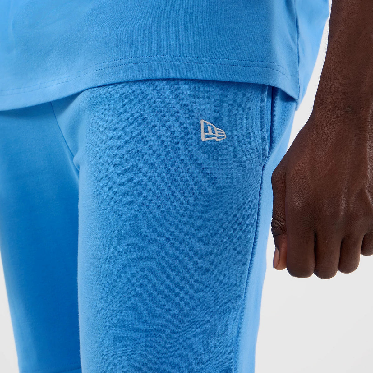 New Era New York Yankees MLB League Essential Pastel Blue Shorts, side view showing the pastel blue colour, a white embroidered New Era logo near the pocket, and worn with a matching blue top, highlighting the casual and coordinated styling.