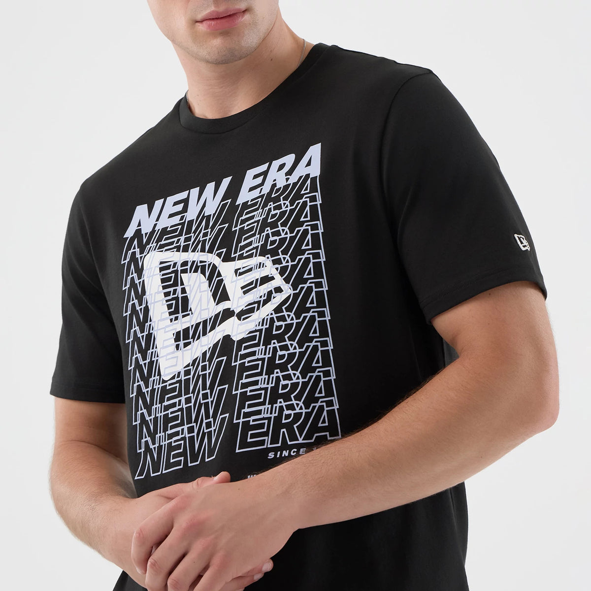 New Era Logo Graphic Black T-Shirt, front view with a large white New Era logo printed over multiple repeating NEW ERA texts creating a dynamic pattern, small embroidered logo on the left sleeve, worn by a model.