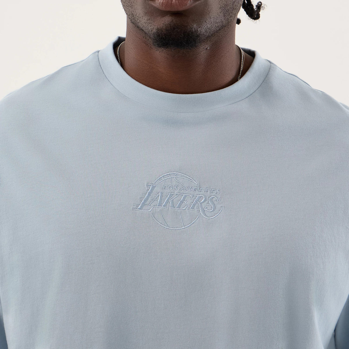 New Era LA Lakers NBA League Essential Pastel Blue Oversized T-Shirt, front view on-model featuring a embroidered Lakers logo centred near the neckline, with broad shoulders and a round neck against a plain background.