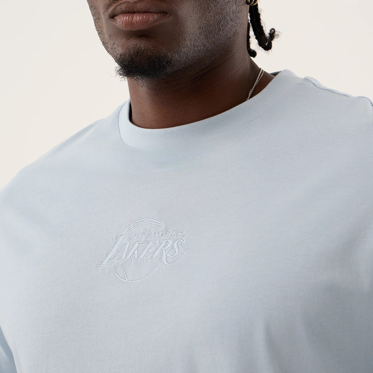 New Era LA Lakers NBA League Essential Pastel Blue Oversized T-Shirt, front view featuring an embroidered Los Angeles Lakers logo in the centre of the chest, short sleeves and a ribbed crew neckline, shown on a model for context and style.
