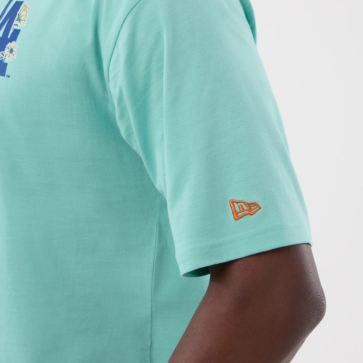 New Era LA Dodgers MLB Floral Pastel Green Oversized T-Shirt, side view showing a detailed floral LA logo on the chest, a pastel green backdrop, and an embroidered orange New Era logo positioned near the sleeve hem.