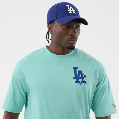 New Era LA Dodgers MLB Floral Pastel Green Oversized T-Shirt, front view on-model showing a blue embroidered LA logo with floral details on the left chest, short sleeves, and a small orange New Era logo embroidered near the left sleeve hem.