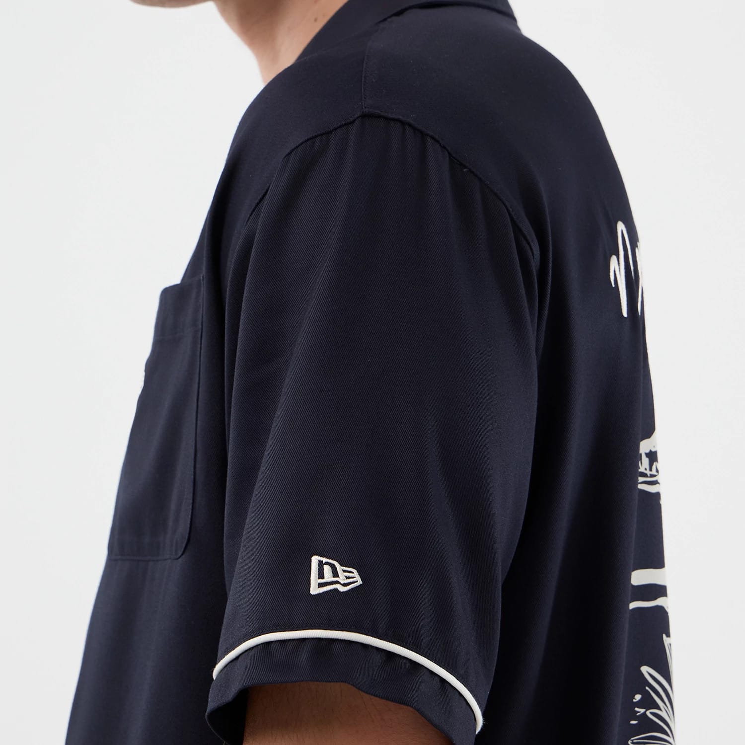 The model is wearing this New Era Graphic Revere Short Sleeve Shirt in navy. 8