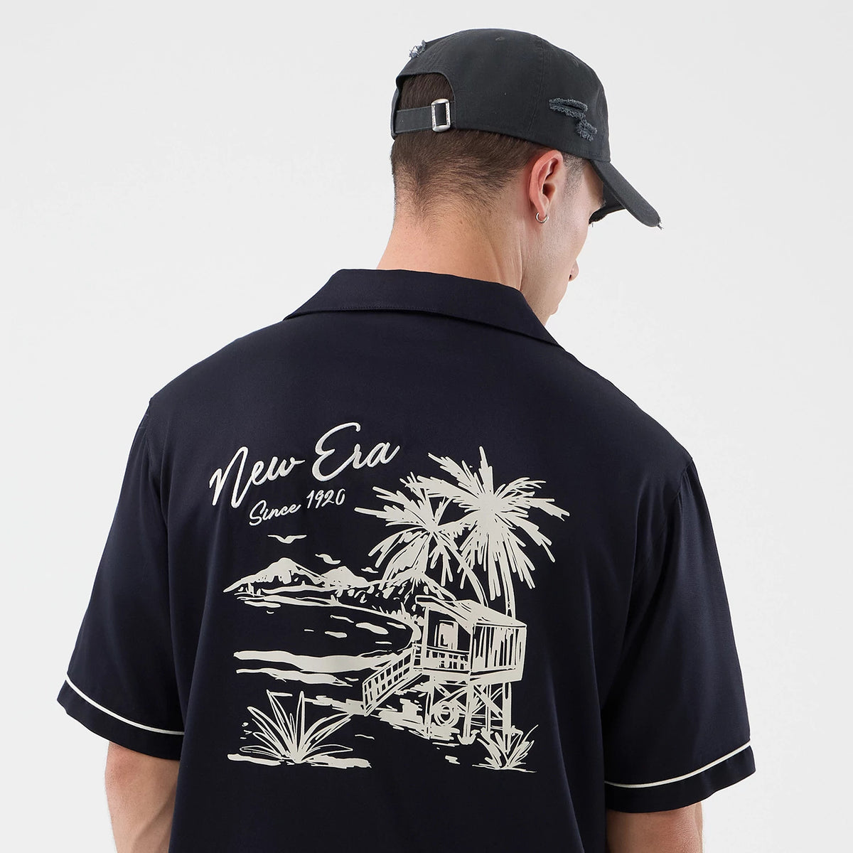 The model is wearing this New Era Graphic Revere Short Sleeve Shirt in navy. 5