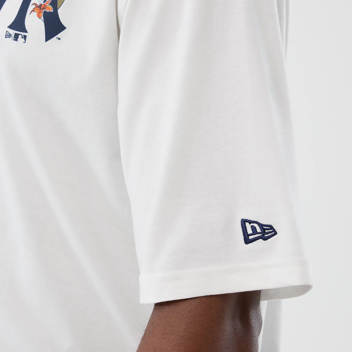New Era New York Yankees MLB Floral White Oversized T-Shirt, side view showing a close-up of the sleeve with a navy embroidered New Era logo near the hem and part of the floral Yankees logo on the upper portion.