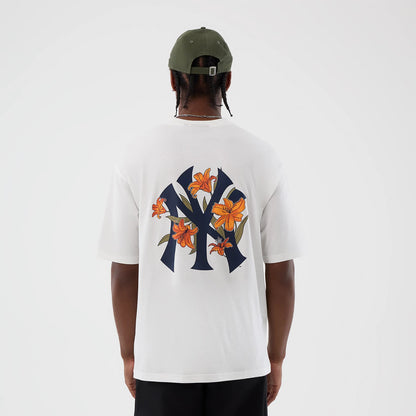 New Era New York Yankees MLB Floral White Oversized T-Shirt, back view on a model showing a large navy Yankees logo with orange floral accents across the back, paired with a green cap and black trousers, highlighting the graphic design.