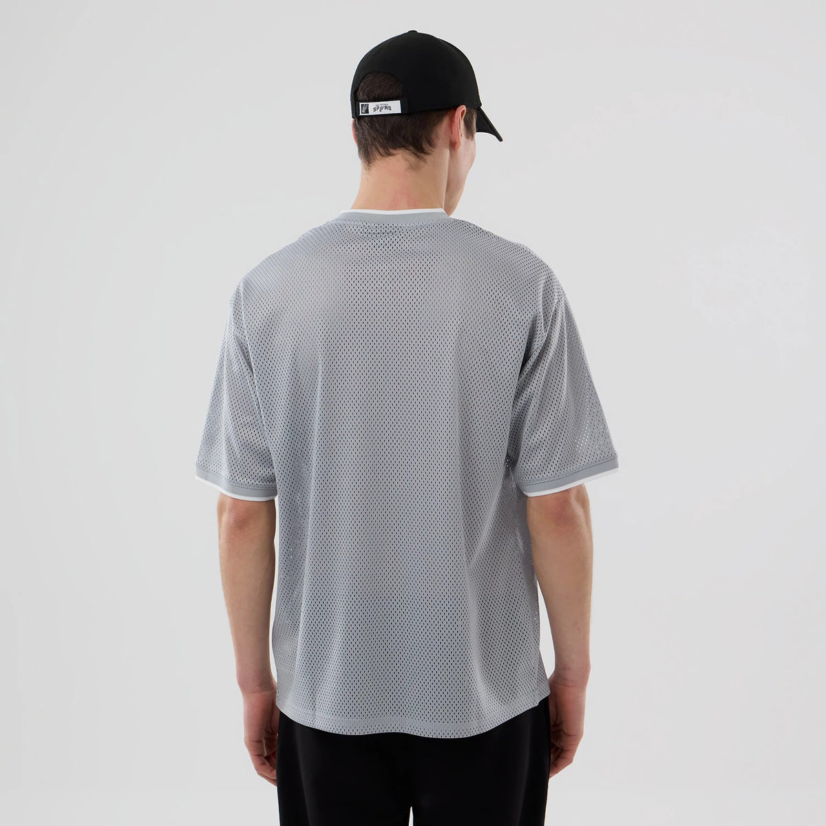 New Era San Antonio Spurs NBA Mesh Grey Oversized T-Shirt, back view on-model showing the textured grey mesh fabric throughout, short sleeves with white trim, and a relaxed fit that complements the black cap worn by the model.