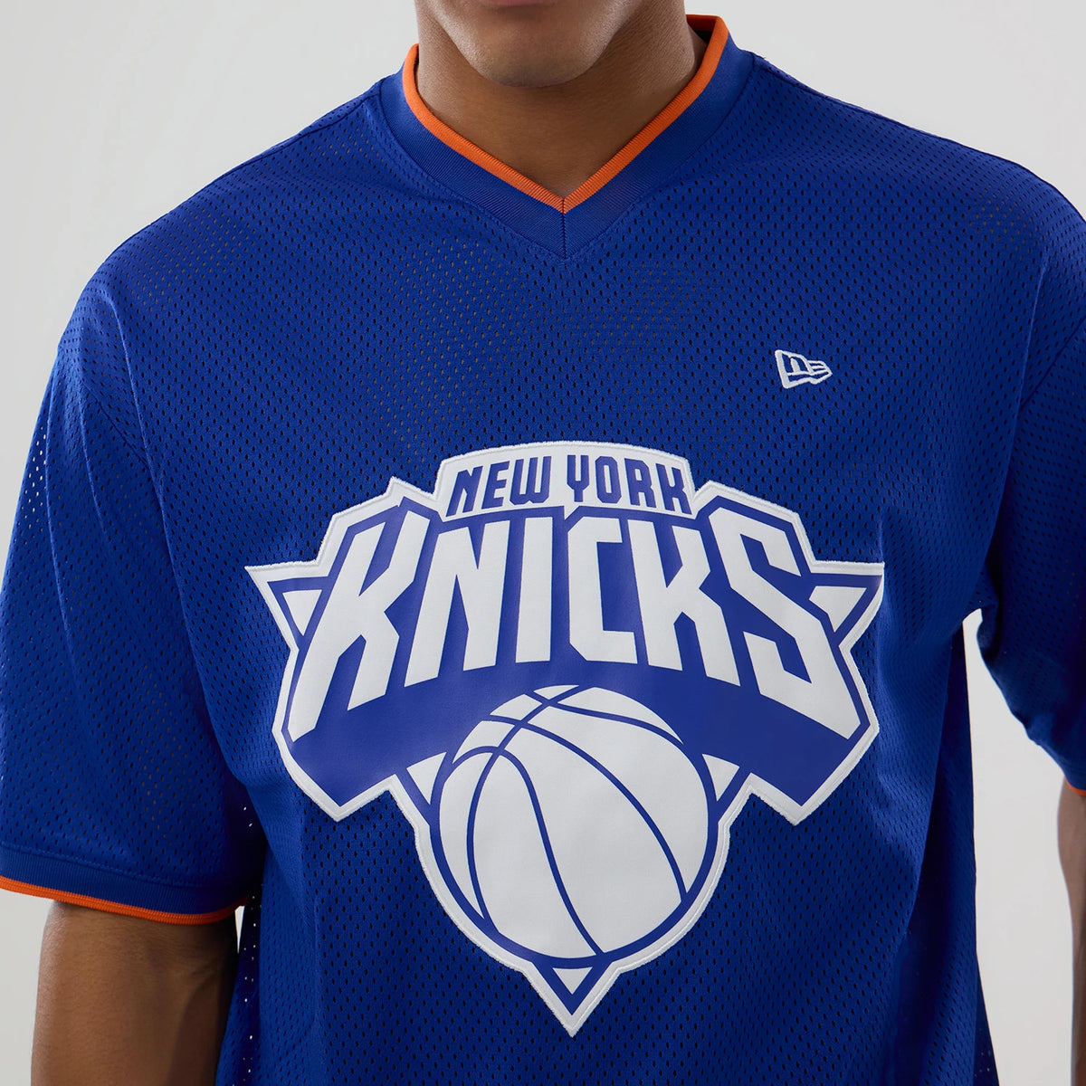 New Era New York Knicks NBA Mesh Blue Oversized T-Shirt, front view showing the large white New York Knicks wordmark and basketball graphic on the chest, an embroidered New Era logo on the upper left chest, and orange trim on the V-neck and sleeves.