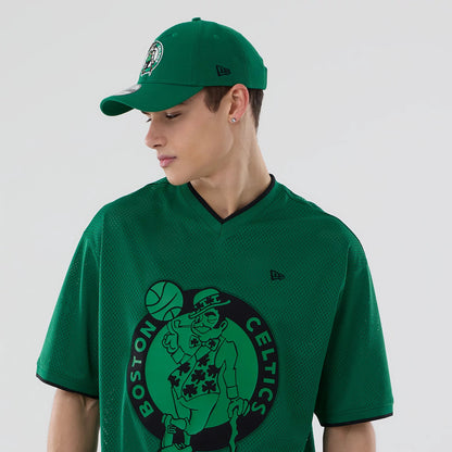 New Era Boston Celtics NBA Mesh Green Oversized T-Shirt, front view on-model showing an oversized green mesh design, with a large printed Celtics logo on the front centre, an embroidered New Era logo on the left sleeve and a black V-neck collar.