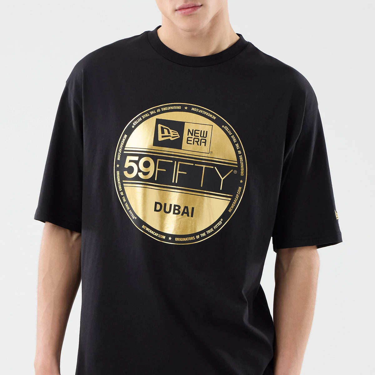 New Era Sticker Dubai Black Oversized T-Shirt, front view on a model with a large gold printed circular graphic featuring the New Era logo, 59FIFTY text, and Dubai wording, short sleeves and a relaxed fit.