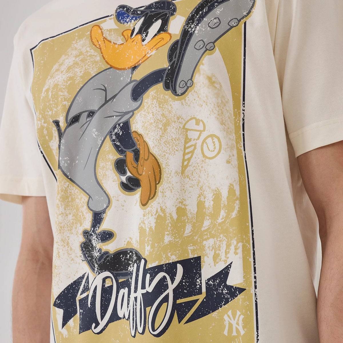 New Era New York Yankees MLB X Looney Tunes Cream T-Shirt, front view featuring a large, distressed graphic of Daffy Duck in a dynamic pose, with his name in lettering below and the embroidered New Era logo in white at the bottom right.