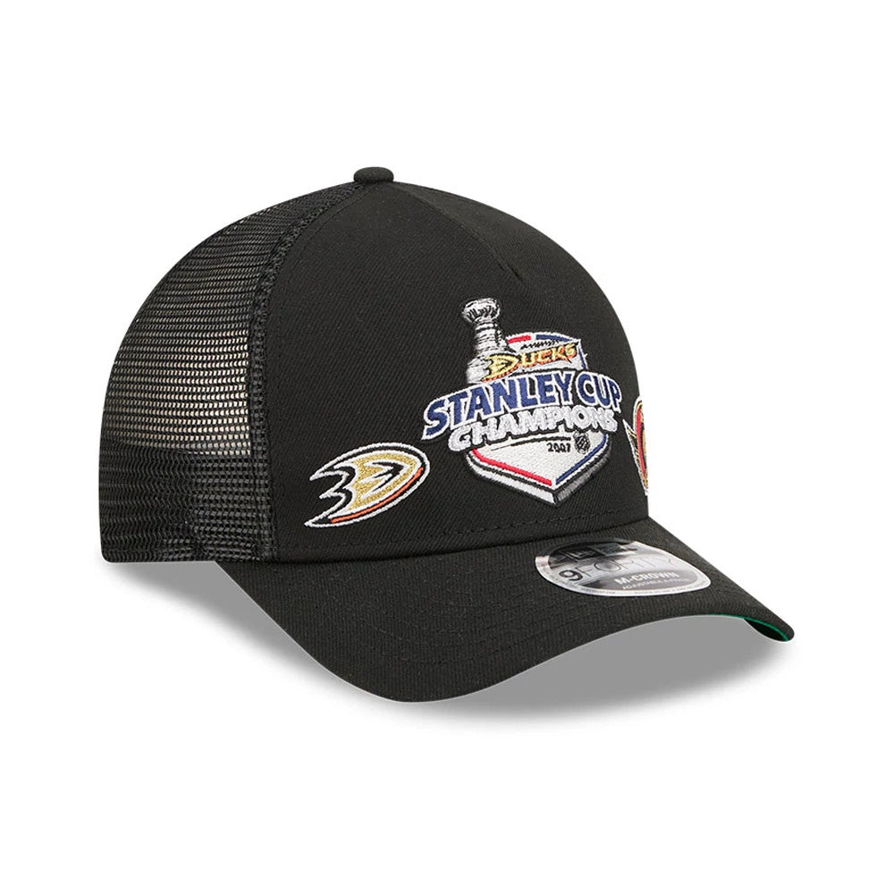 Ducks NHL Stanley Cup Black New Era 9FORTY M-Crown A-Frame Trucker Adjustable Cap, three-quarter view showing the embroidered Stanley Cup Champions graphic and Ducks logo on the front panel, black mesh back panels.