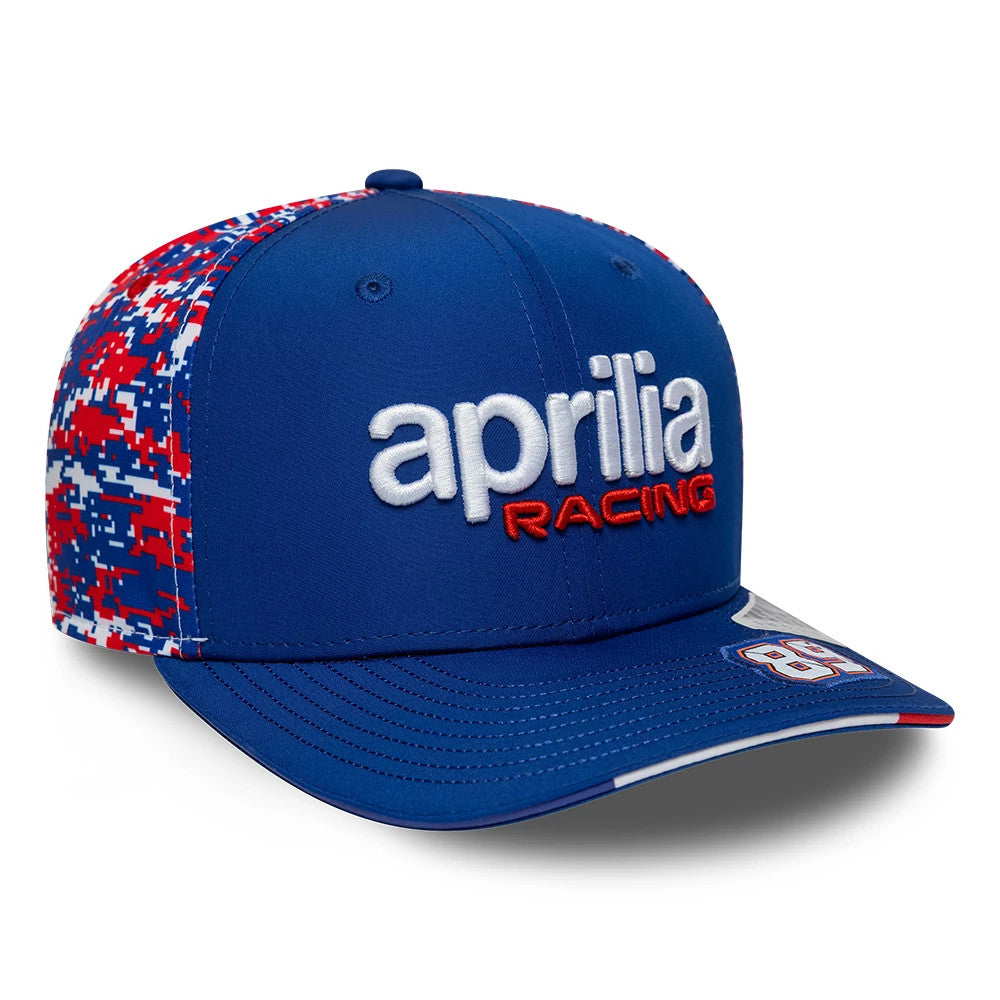 Aprilia Replica Jorge Martin Le Mans Race Special Blue New Era 9SEVENTY Stretch Snap Adjustable Cap, three-quarter view showing the white and red embroidered aprilia racing logo on the front panel, red and blue digital camo pattern on side panels.