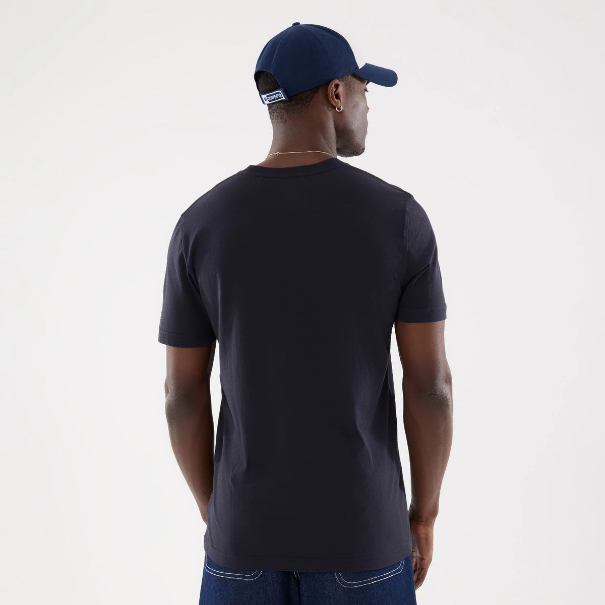 New Era Dallas Cowboys NFL Training 2026 Navy T-Shirt, back view on a model wearing a navy cap, showing a plain navy back with short sleeves and the shirt's relaxed fit, paired with dark jeans for a casual style.