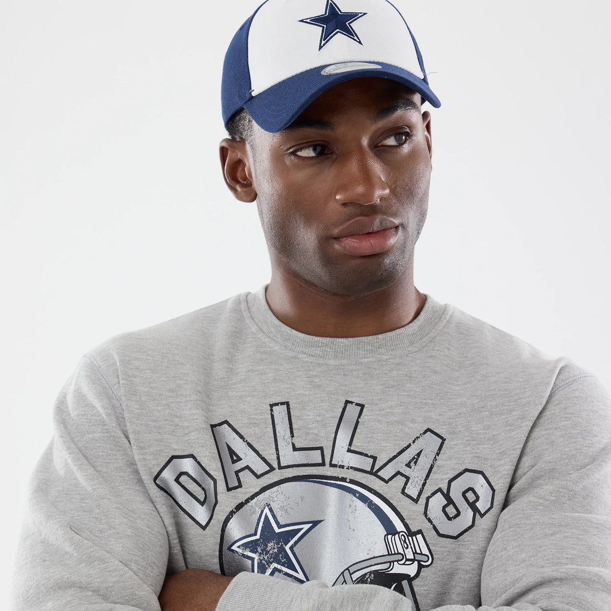 New Era Dallas Cowboys NFL Training 2026 Grey Crew Neck Sweater, on-model view with the model wearing a grey sweater featuring a distressed Dallas Cowboys helmet graphic across the chest and black lettered design.