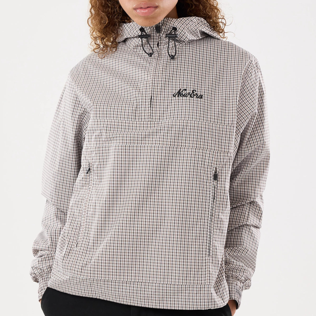 Womens New Era Check Beige Oversized Windbreaker Jacket, front view on-model showcasing a beige checked pattern with an embroidered New Era logo on the chest, a half-zip design with drawcords at the hood, and zipped pockets on each side.