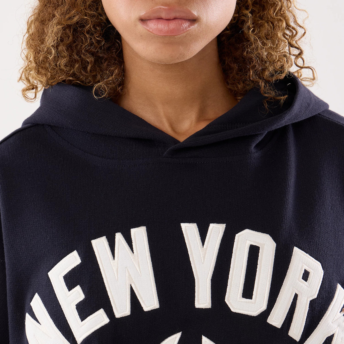 New Era New York Yankees Womens MLB Navy Oversized Pullover Hoodie, front view on-model featuring large white embroidered lettering spelling New York across the chest, with a dark navy colour and a relaxed hood draped casually.
