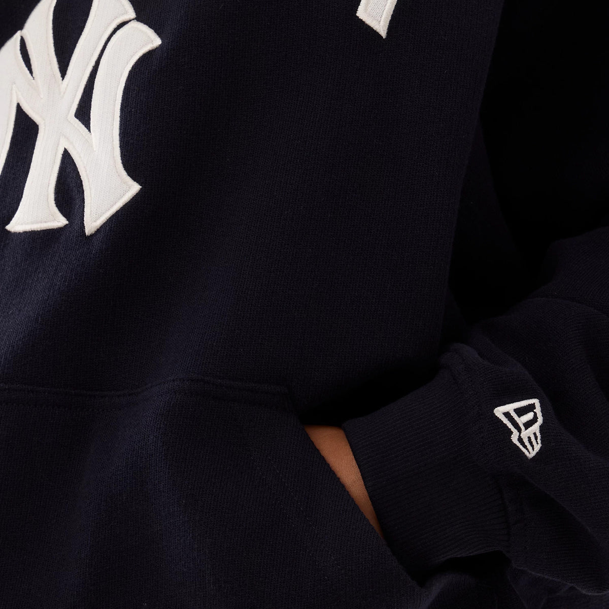 New Era New York Yankees Womens MLB Navy Oversized Pullover Hoodie, front view featuring a large white embroidered NY logo on the chest, a hand in the kangaroo pocket, and a small embroidered New Era flag logo on the left cuff.
