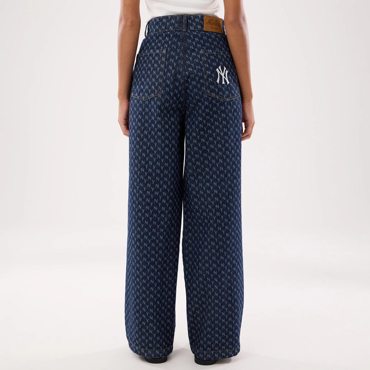 New Era New York Yankees Womens MLB Denim Navy Wide Leg Trousers, back view on a model showing a white embroidered NY logo on the back pocket, an all-over repeating pattern, and a New Era leather patch above the waistband.