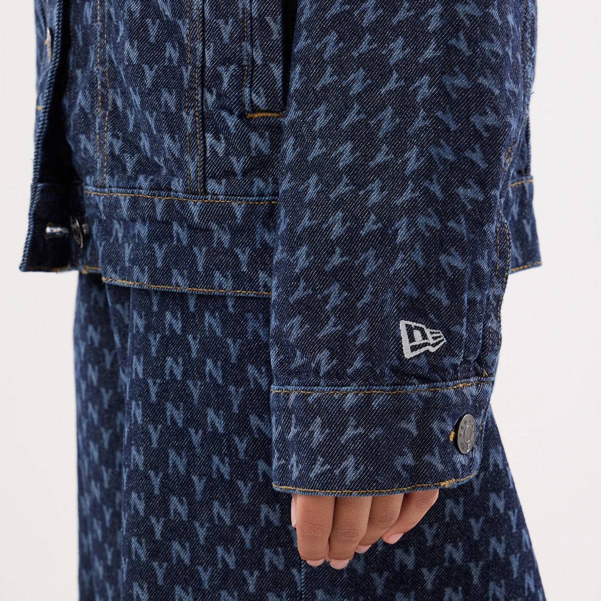 New Era New York Yankees Womens MLB Denim Navy Jacket, side view showing a close-up of the sleeve with an all-over navy and light blue N pattern, a white embroidered New Era logo near the cuff, and a button detail at the wrist.