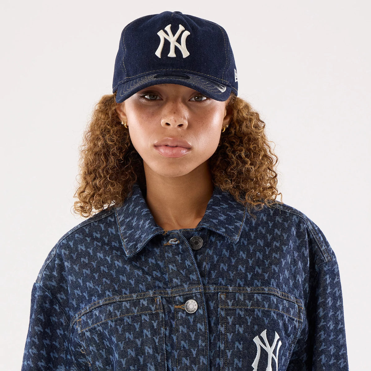 New Era New York Yankees Womens MLB Denim Navy Jacket, front view on a model wearing a matching cap, showcasing a patterned navy jacket with an embroidered Yankees logo on the left chest and silver buttons down the front.