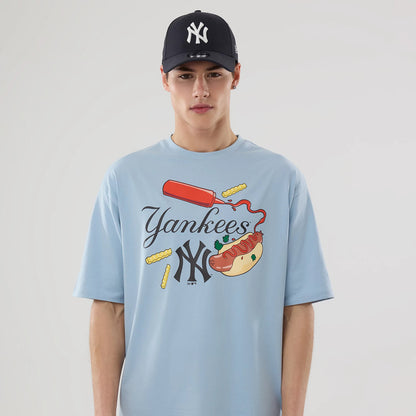 New Era New York Yankees MLB Food Graphic Pastel Blue Oversized T-Shirt, front view on a model featuring a ketchup bottle and hot dog graphic with fries, complemented by embroidered Yankees lettering.