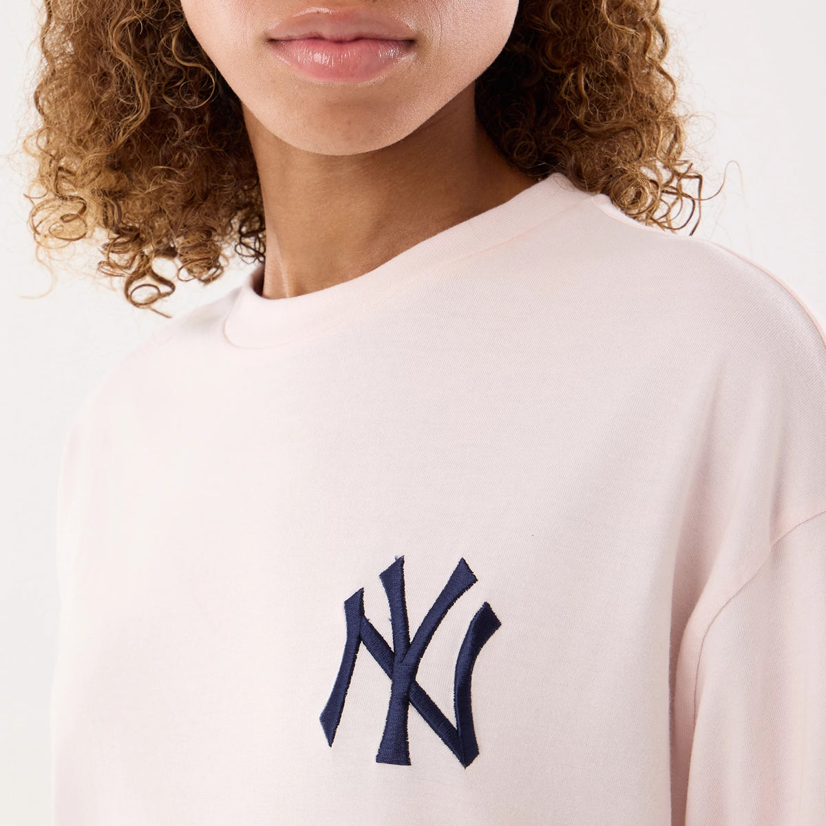 New Era New York Yankees Womens MLB Graphic Pastel Pink T-Shirt, front view on-model featuring a dark blue embroidered NY logo on the left chest, and a casual round neckline against the soft pastel pink fabric.