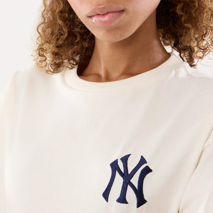 New Era New York Yankees Womens MLB Graphic Open Cream T-Shirt, front view on a model showing a close-up of the navy blue embroidered NY logo on the left chest, with a cream fabric and a simple round neckline.