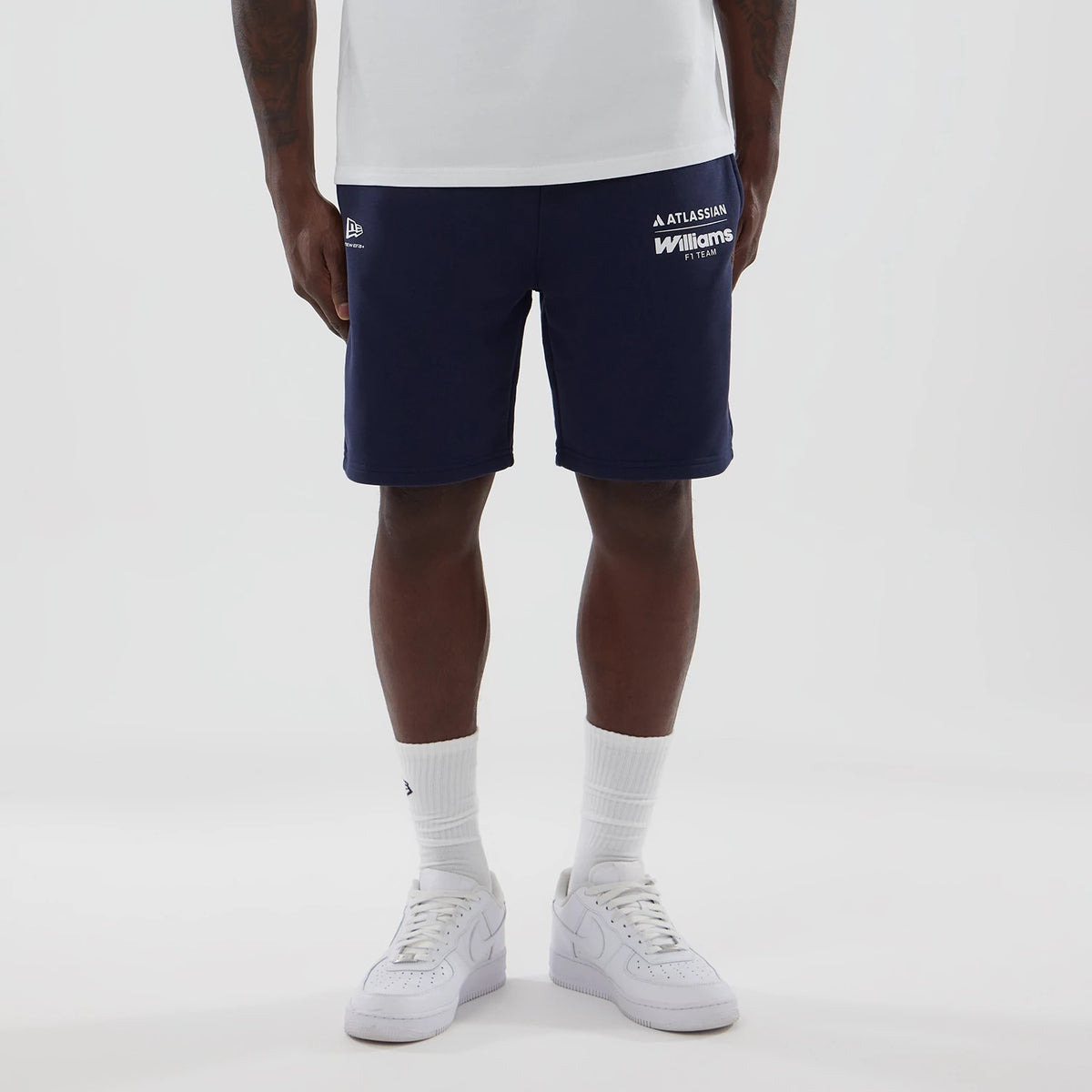 New Era Williams Navy Shorts, front view on-model, showcasing the navy colour with white printed team logos on the left side, the New Era logo embroidered on the opposite side, paired with a plain white t-shirt and matching white trainers.