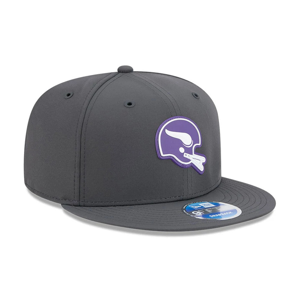 Vikings NFL Sideline 2026 Charcoal New Era 9FIFTY Snapback Adjustable Cap, three-quarter view showing a purple and white Vikings helmet logo on the front panel, a flat charcoal visor with a blue and white 9FIFTY size sticker, and black eyelets.