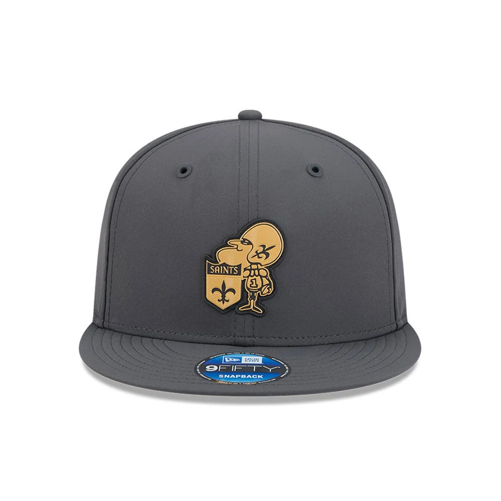 Saints NFL Sideline 2026 Charcoal New Era 9FIFTY Snapback Adjustable Cap, front view showing a gold embroidered Saints mascot and shield logo on the front panel, with a dark charcoal visor and a 9FIFTY size sticker on the visor.