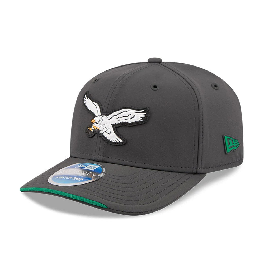 Eagles NFL Sideline 2026 Charcoal New Era 9SEVENTY Stretch Snap Adjustable Cap, three-quarter view showing the white embroidered eagle logo on the front panel, a green New Era flag logo on the left side and a grey visor with a 9SEVENTY size sticker.