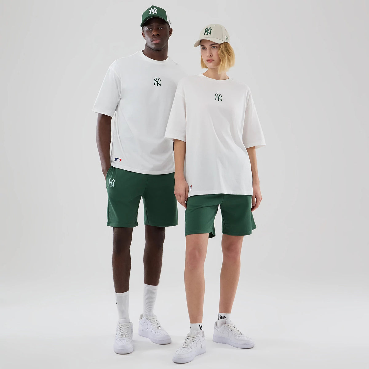 New Era New York Yankees MLB Midi League Essential White Oversized T-Shirt, front view on-model showcasing the distinctive green embroidered Yankees logo on the chest, paired with green shorts and caps, with a small embroidered MLB logo near the hem.