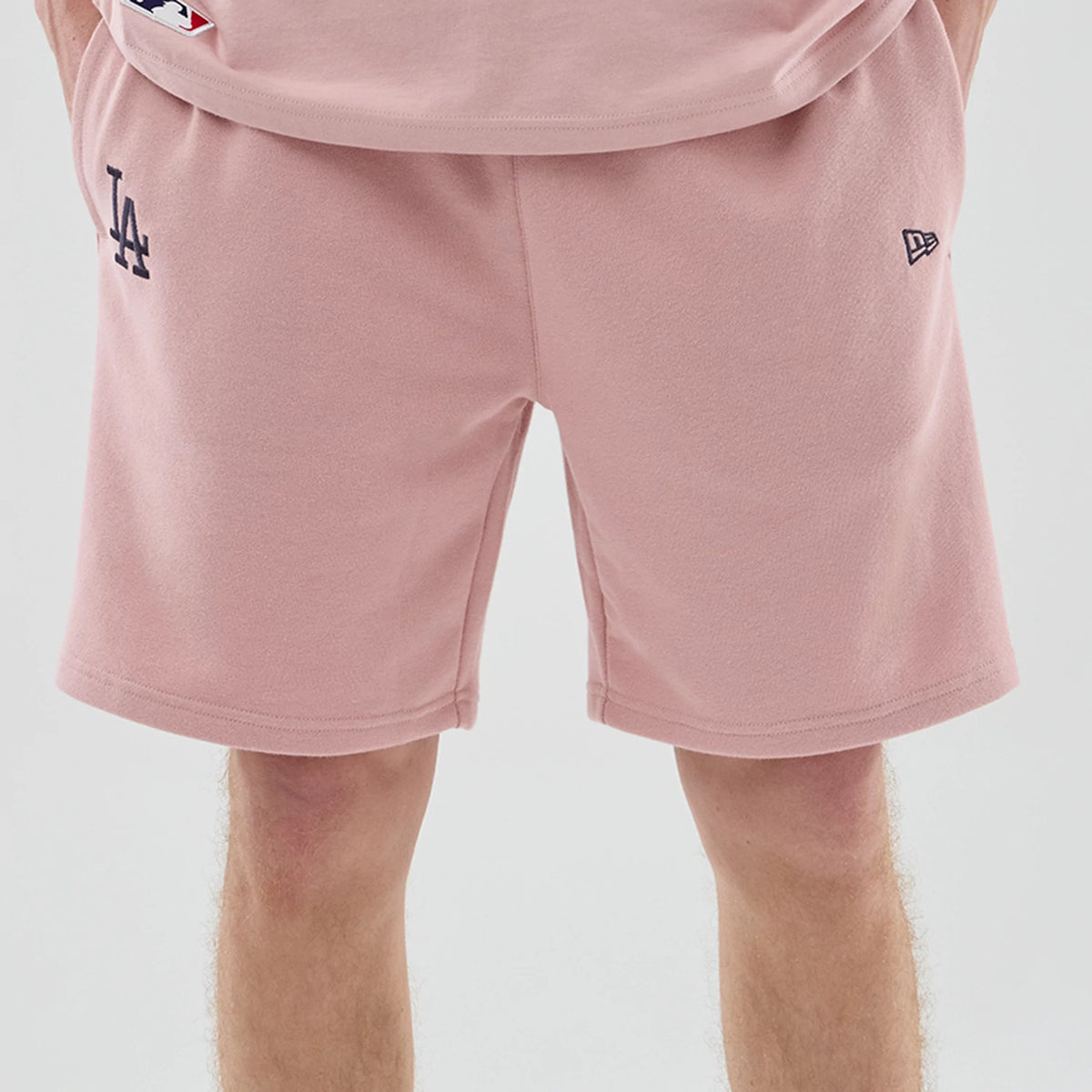 New Era LA Dodgers MLB Midi League Essential Pastel Pink Oversized Shorts, front view on a model showing a navy embroidered LA logo on the left leg, with the New Era flag embroidered on the right, and relaxed fit knee-length legs.