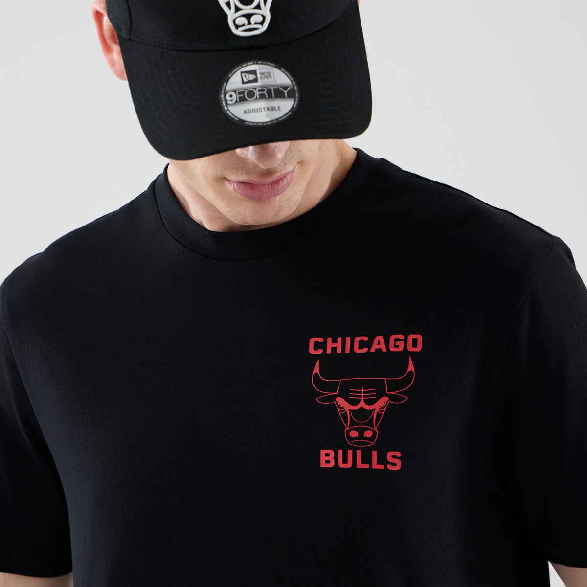 New Era Chicago Bulls NBA Court Graphic Black T-Shirt, front view on-model featuring a red printed Chicago Bulls logo and lettering on the left chest, paired with a black cap with a contrasting raised logo above the curved visor.
