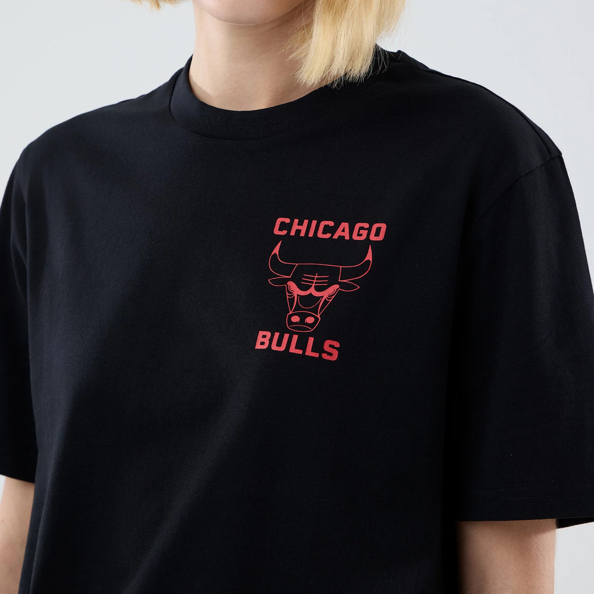 New Era Chicago Bulls NBA Court Graphic Black T-Shirt, three-quarter view showing the red printed Chicago Bulls logo and lettering on the left chest, worn by a model with blonde hair, highlighting the relaxed fit and classic round neckline.