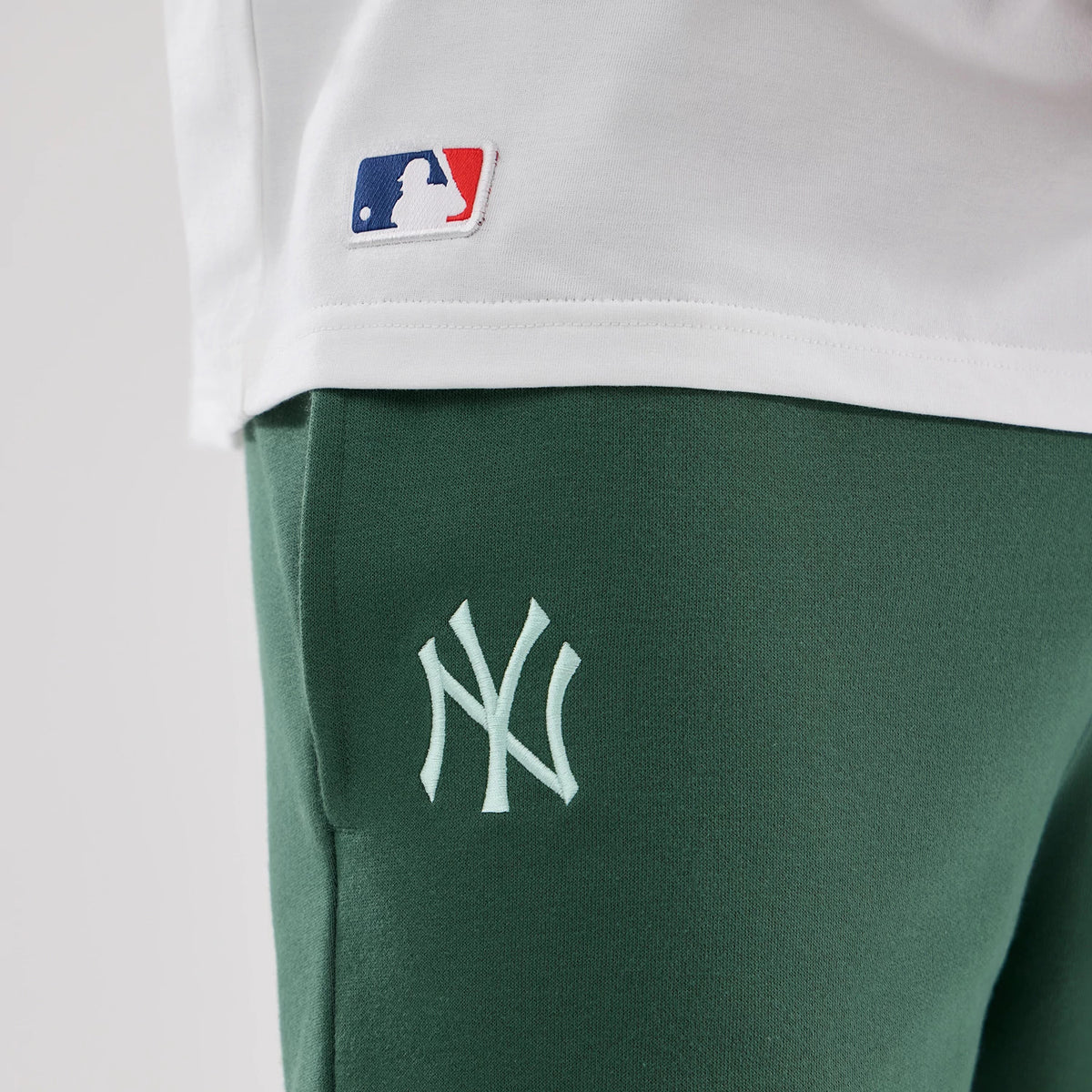 New Era New York Yankees MLB Midi League Essential Dark Green Oversized Shorts, close-up view showing the white embroidered New York Yankees logo on the left thigh, contrasted against the dark green fabric.