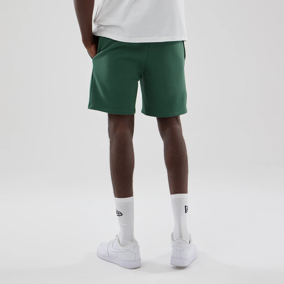 New Era New York Yankees MLB Midi League Essential Dark Green Oversized Shorts, back view on a model wearing a white T-shirt, highlighting the relaxed fit of the dark green shorts with side pockets, paired with white trainers.