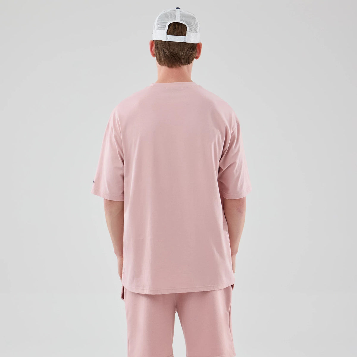 New Era LA Dodgers MLB Midi League Essential Pastel Pink Oversized T-Shirt, back view on a model wearing matching pink shorts, showing plain pastel pink fabric with a relaxed, loose fit and a small embroidered New Era logo on the left sleeve.