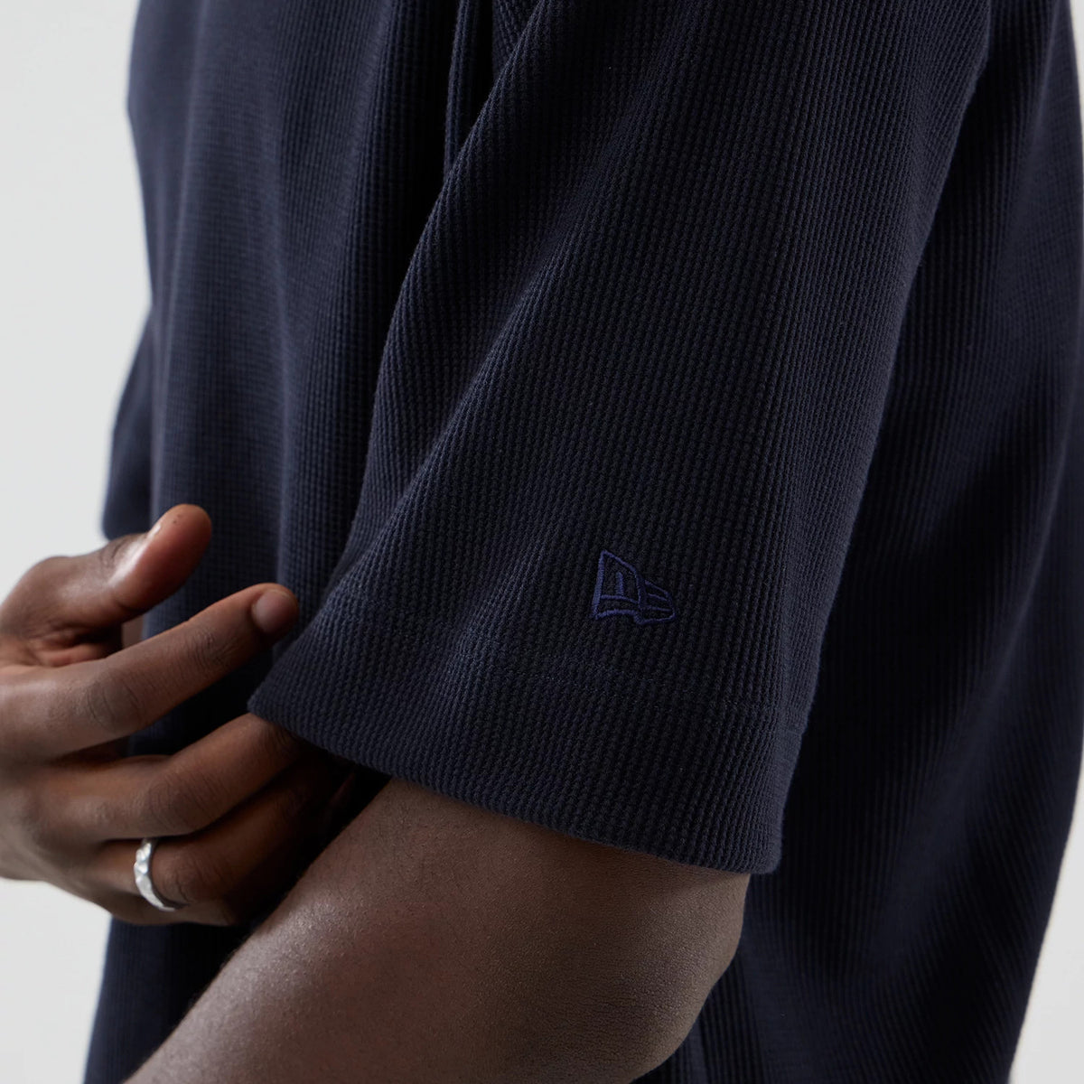 New Era Waffle Navy Boxy T-Shirt, side view showing the textured waffle pattern of the navy fabric with an embroidered New Era logo near the sleeve hem, as a model's hand lightly adjusts the short sleeve edge.