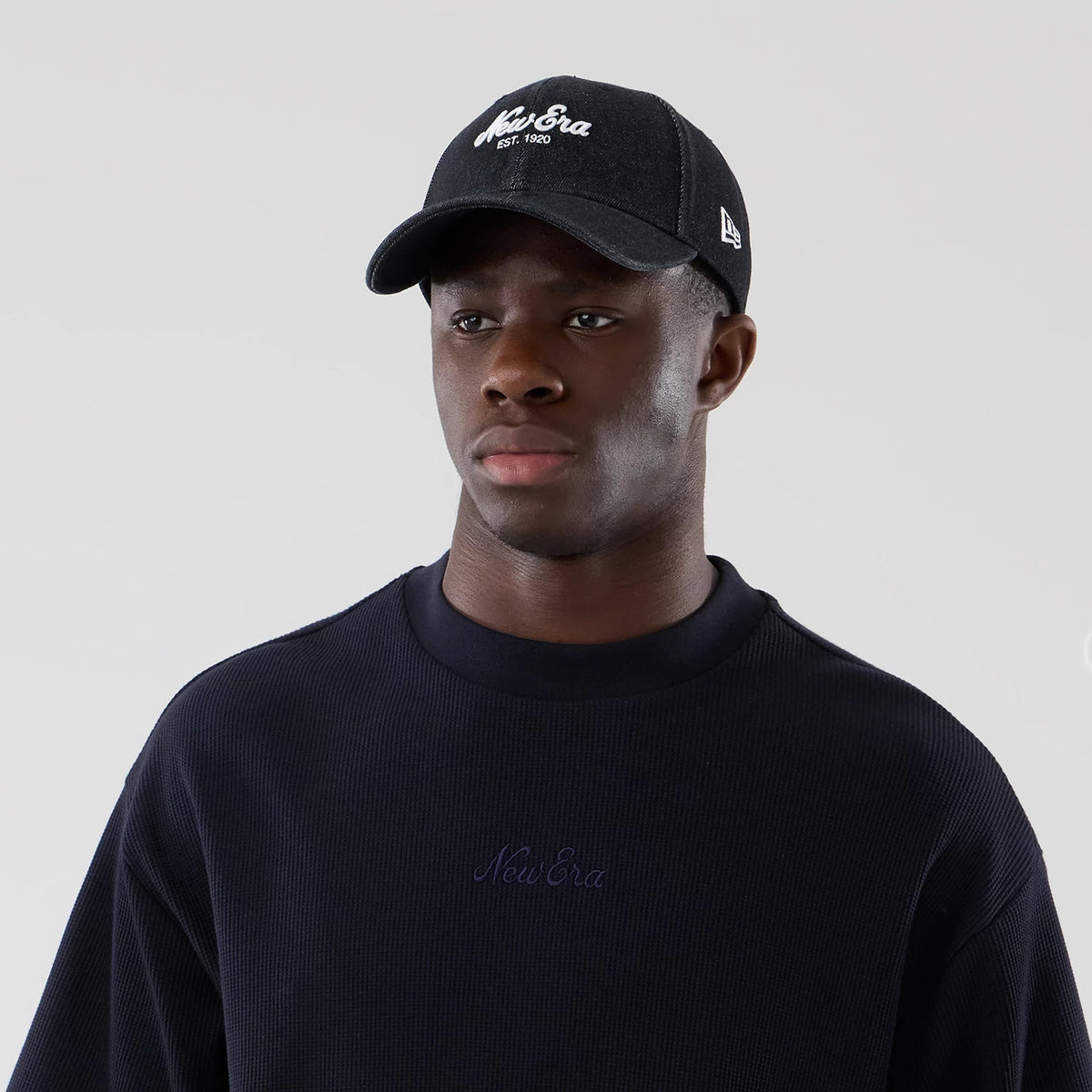 New Era Waffle Navy Boxy T-Shirt, front view on-model paired with a black cap, showcasing an embroidered New Era logo centrally on the chest of the navy waffle-textured fabric, highlighting the crew neck and relaxed boxy fit.
