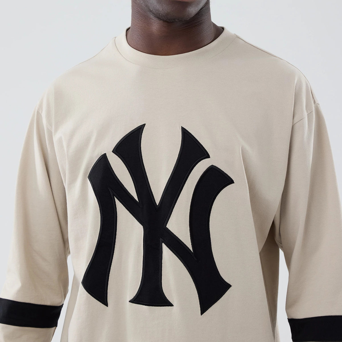 New Era New York Yankees MLB Light Beige Oversized Long Sleeve T-Shirt, front view displaying a large black embroidered Yankees logo centred on the chest, with black stripe around the forearms on both sleeves, worn by a model.