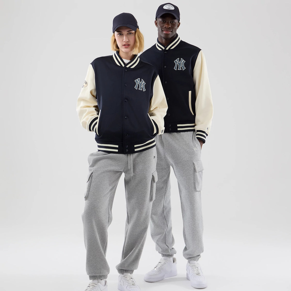New Era New York Yankees MLB Jersey Bomber Navy Jacket, front view on models showcasing the navy body with the white embroidered Yankees logo on the chest, contrasting cream sleeves, and striped navy and cream ribbed cuffs, hem, and collar.