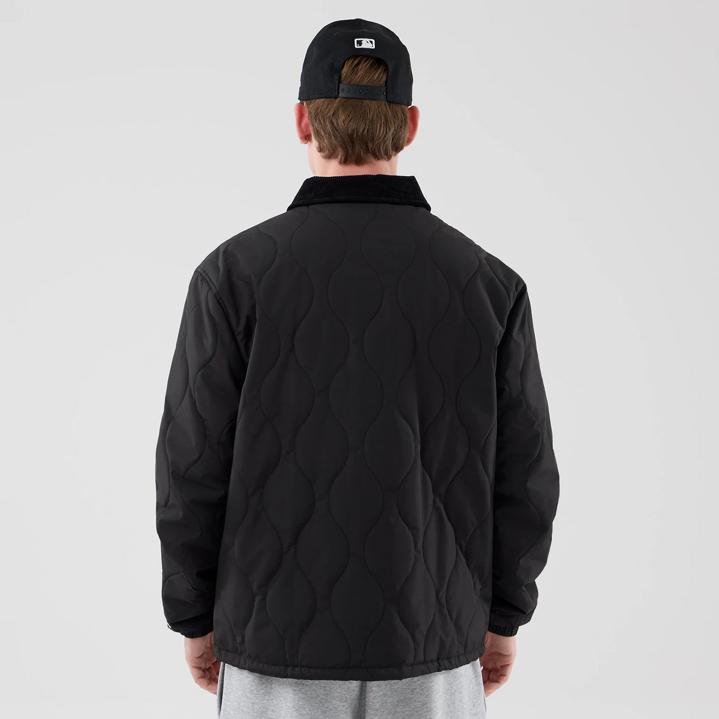 The model is wearing this New Era Quilted Coaches Jacket in black. 2