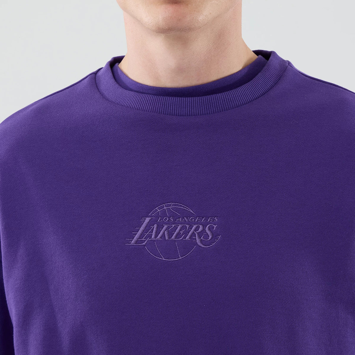 New Era LA Lakers NBA League Essential Purple Oversized Crew Neck Sweater, front view on a model showing the purple embroidered Los Angeles Lakers logo on the left chest, with a ribbed crew neck and a purple fabric.