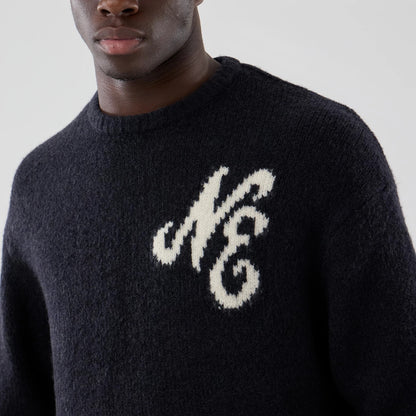 New Era Knit Heritage Navy Knitted Sweater, front view on a model showing the textured navy fabric with a large white embroidered script NE logo on the left chest, featuring a thick ribbed crew neck.