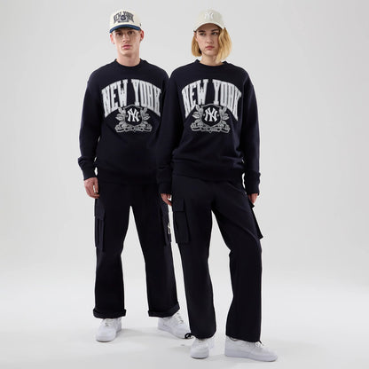 New Era New York Yankees MLB Arch Graphic Navy Oversized Crew Neck Sweater, front view on models with matching caps, displaying a large white New York text above the Yankees logo on the navy fabric, paired with black cargo trousers.