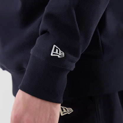 New Era New York Yankees MLB Arch Graphic Navy Oversized Crew Neck Sweater, close-up view with the New Era flag logo embroidered in white on the sleeve cuff, showing the thick ribbed fabric and relaxed fit on a model.