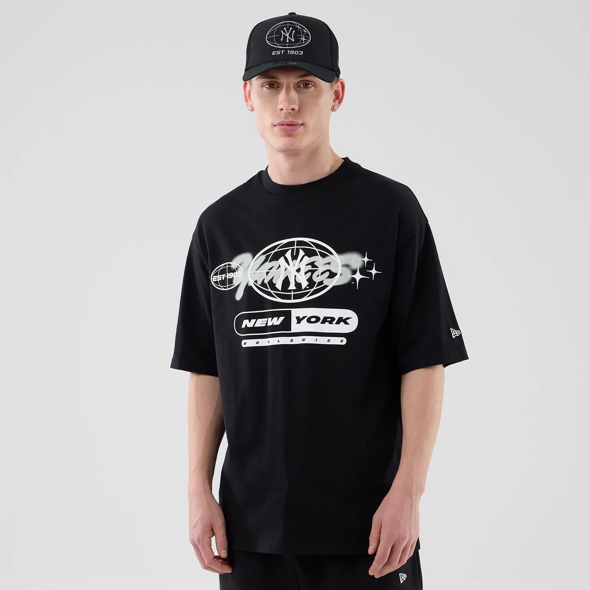 New Era New York Yankees MLB Logo Graphic Black Oversized T-Shirt, front view on a model wearing a matching cap, showcasing a large white printed graphic with the New York Yankees emblem across the chest.